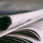 Stack of folded newspapers on a wooden table with a focus on printed pages.