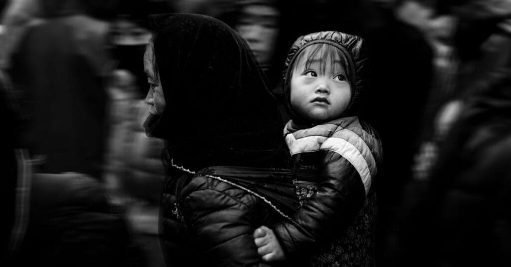 Captivating black and white street photo capturing a mother carrying her child through a bustling crowd.