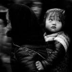 Captivating black and white street photo capturing a mother carrying her child through a bustling crowd.