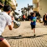 Children running a street race while a man with a megaphone cheers them on.