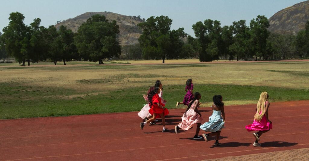 A group of girls wearing colorful dresses running on a track outdoors with hills in the background.