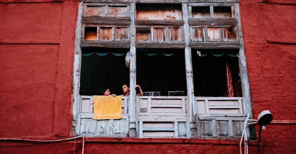 Children looking out of a rustic window with colorful walls in Lahore, capturing daily life.