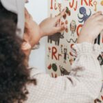A young girl interacting with a colorful alphabet poster at home.