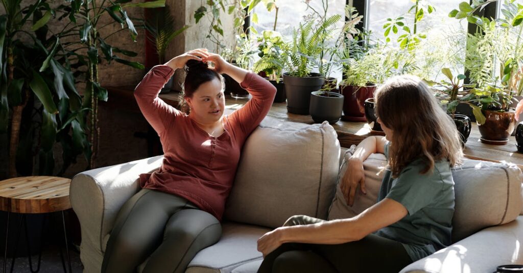 Two women enjoying a relaxed conversation on a sofa in a bright room filled with plants.