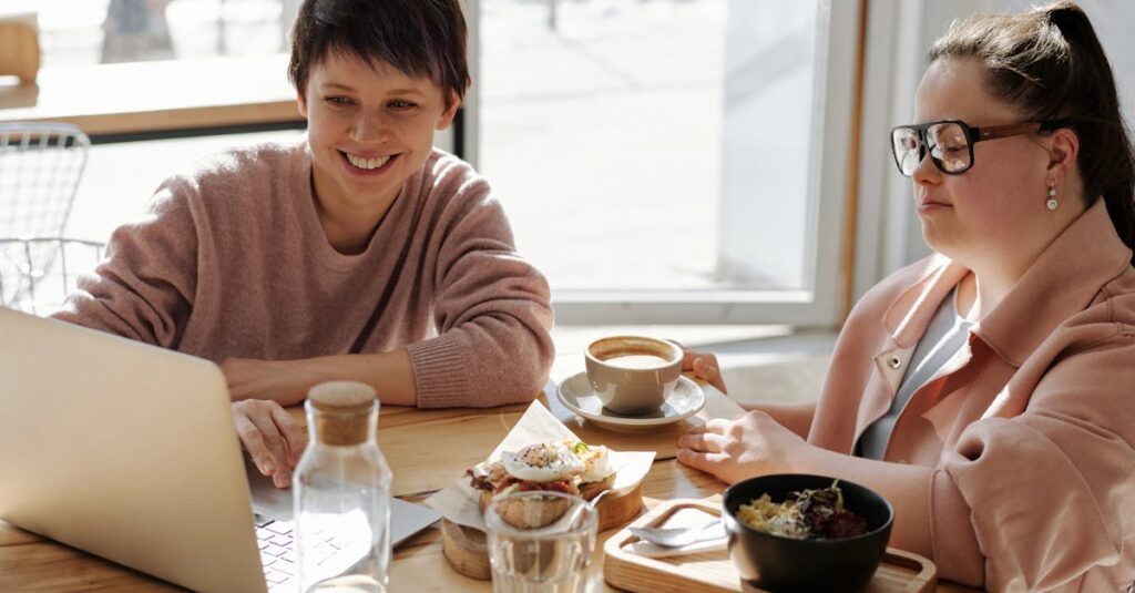 Two women enjoying coffee and snacks while working on a laptop in a bright café setting.