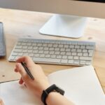 Student attending virtual class on a computer, taking notes at home.