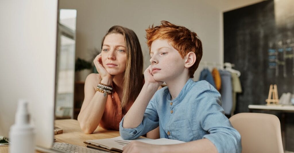 A mother and son engaged in online learning at home using a computer, focusing intently on the screen.
