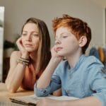 A mother and son engaged in online learning at home using a computer, focusing intently on the screen.
