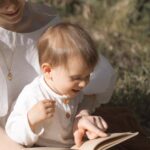 A mother and toddler enjoy reading together in a sunny outdoor setting.