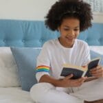 Cheerful girl enjoys reading in bright, cozy bedroom. Warm and inviting indoor scene.