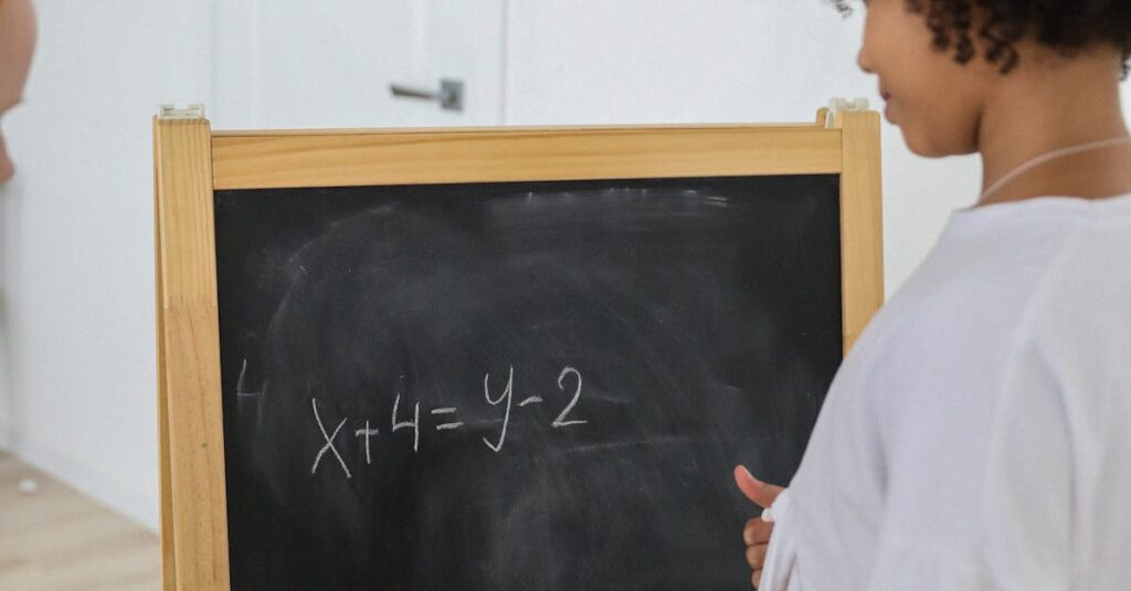Back view of African American girl writing numbers and symbols on chalkboard in classroom