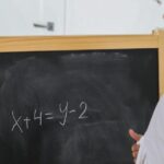 Back view of African American girl writing numbers and symbols on chalkboard in classroom