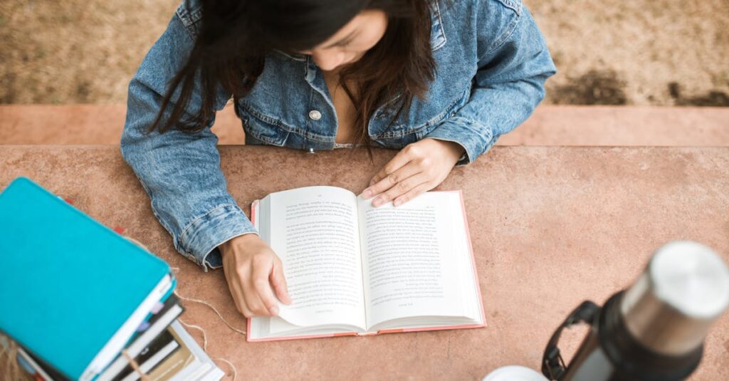 Overhead view of a woman reading a book outdoors on a sunny day, wearing a denim jacket.