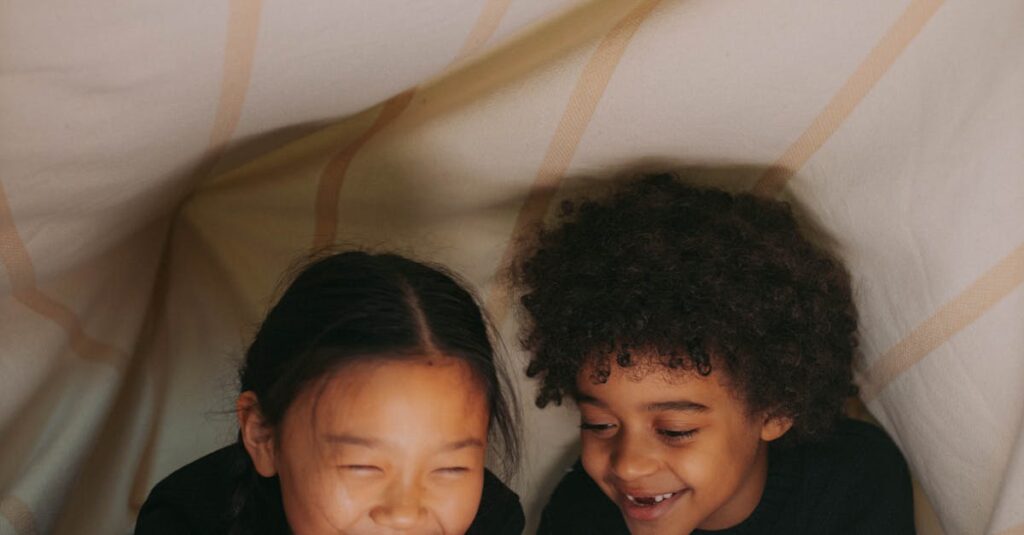 Two children happily reading under a cozy blanket fort with warm lighting.