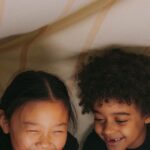 Two children happily reading under a cozy blanket fort with warm lighting.