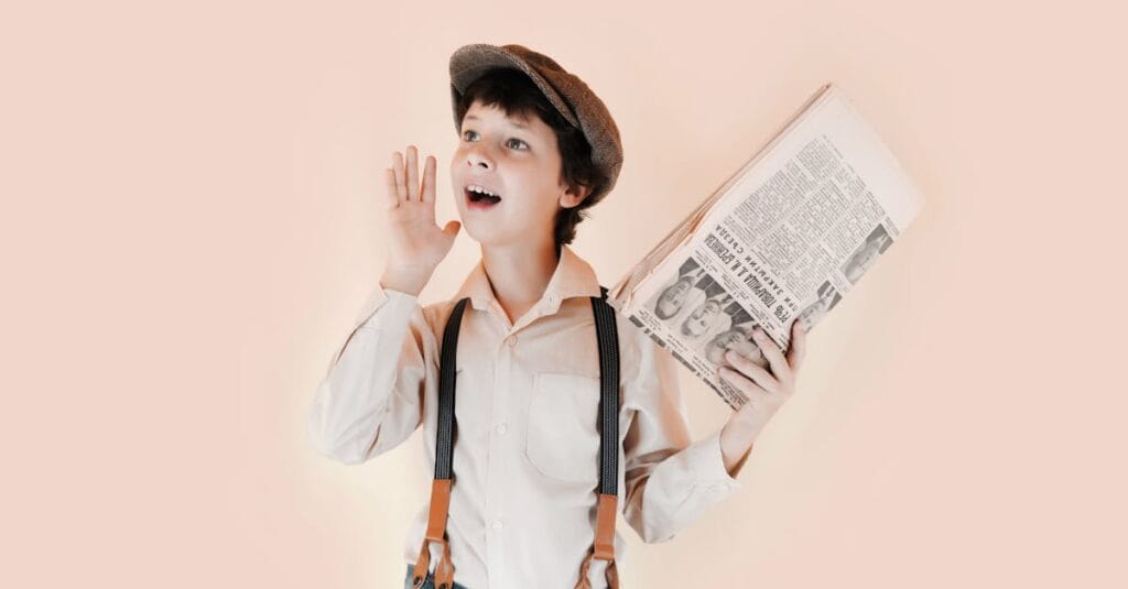 Positive boy in retro clothes holding old newspaper and standing with open mouth and raised arm against beige background in studio