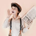 Positive boy in retro clothes holding old newspaper and standing with open mouth and raised arm against beige background in studio