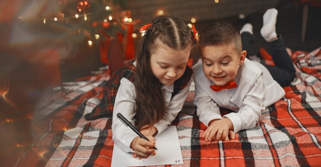 Two children writing letters on a cozy blanket by a decorated Christmas tree.