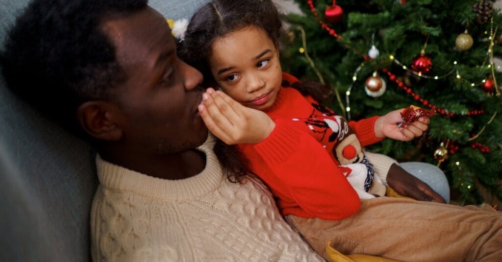 Father and daughter sharing a tender moment by the Christmas tree, enjoying the festive atmosphere.