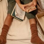 Child sitting under blanket sorting greeting cards, cozy setting indoors.