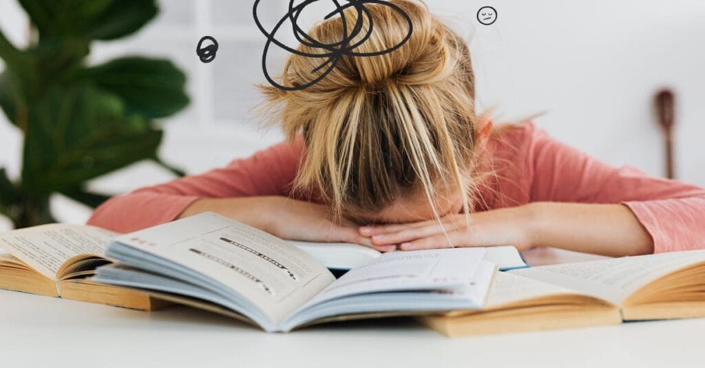 Young woman asleep over books at desk, conveying stress and mental overload.