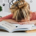 Young woman asleep over books at desk, conveying stress and mental overload.