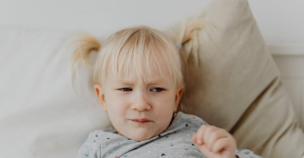A young blonde child with a displeased facial expression on a light background.