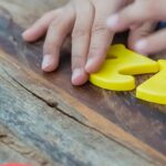 A child arranges colorful plastic numbers on a wooden table, aiding early math education.