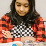 A focused young girl reading a book at her desk in a classroom setting.