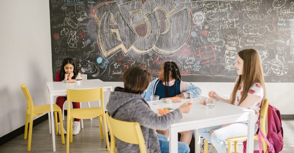 Children sitting in a school classroom having lunch with a chalkboard full of doodles behind them.