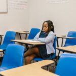 A young girl sits alone in a classroom, depicting isolation and contemplation.