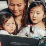 Mother and two children reading a book together, fostering closeness and learning at home.