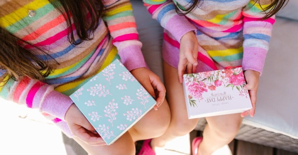 Two children in striped sweaters hold decorative gift boxes. Bright and joyful scene.