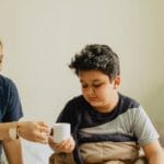 A nurturing mother hands her son a cup in a cozy morning setting.