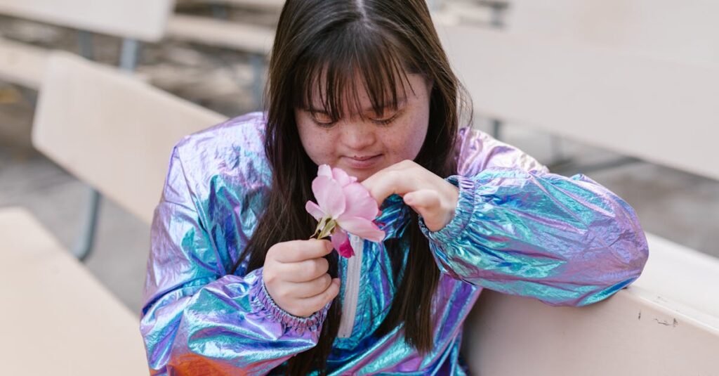 Young girl with Down syndrome in an iridescent jacket holding a pink flower outdoors.