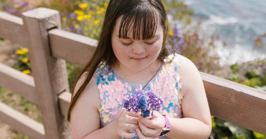 A young girl with Down syndrome enjoys nature, holding purple flowers by a wooden fence.
