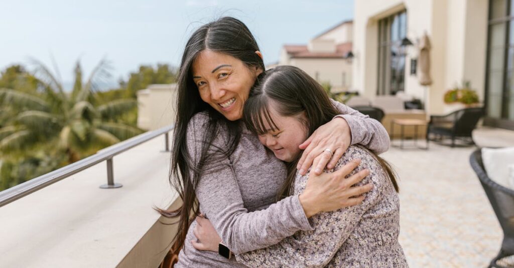 Mother and daughter with Down syndrome share a warm embrace outdoors on a sunny day.