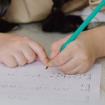 A young girl lying on the floor writing on a music sheet with a pencil indoors.
