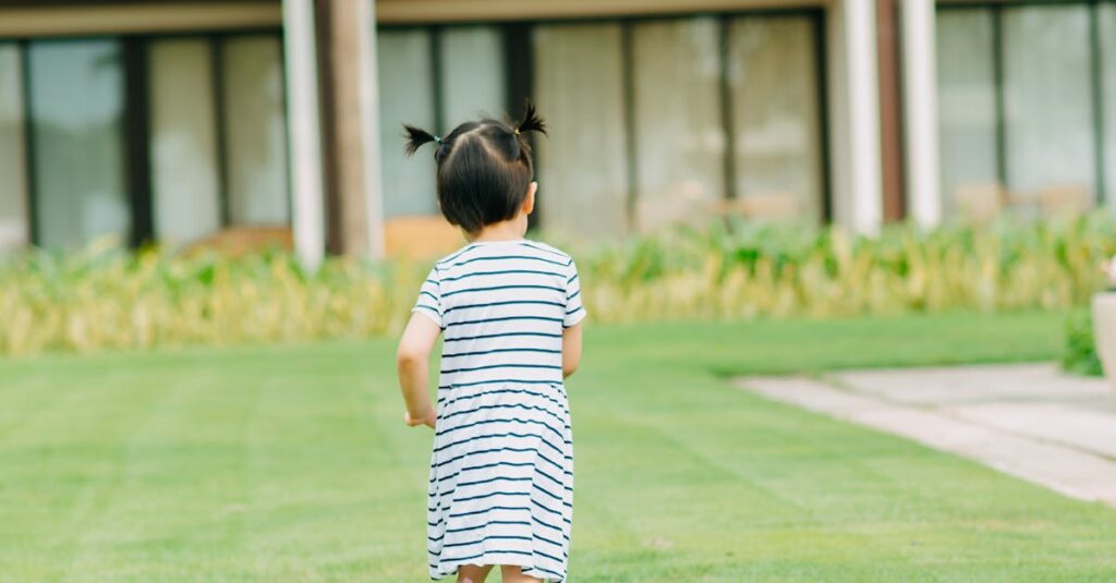 Full body of little girl with cute ponytails running on lawn with verdant fresh grass on blurred background