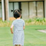 Full body of little girl with cute ponytails running on lawn with verdant fresh grass on blurred background