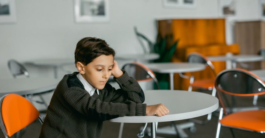 Young boy sitting alone at a table indoors, looking contemplative.