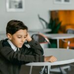 Young boy sitting alone at a table indoors, looking contemplative.
