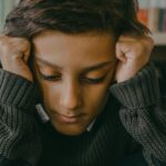 A distressed child sits on the floor in a library with books in the background, embodying sadness.
