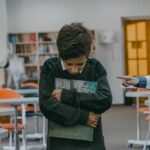 A sad child walks alone in a classroom, facing bullying from classmates.
