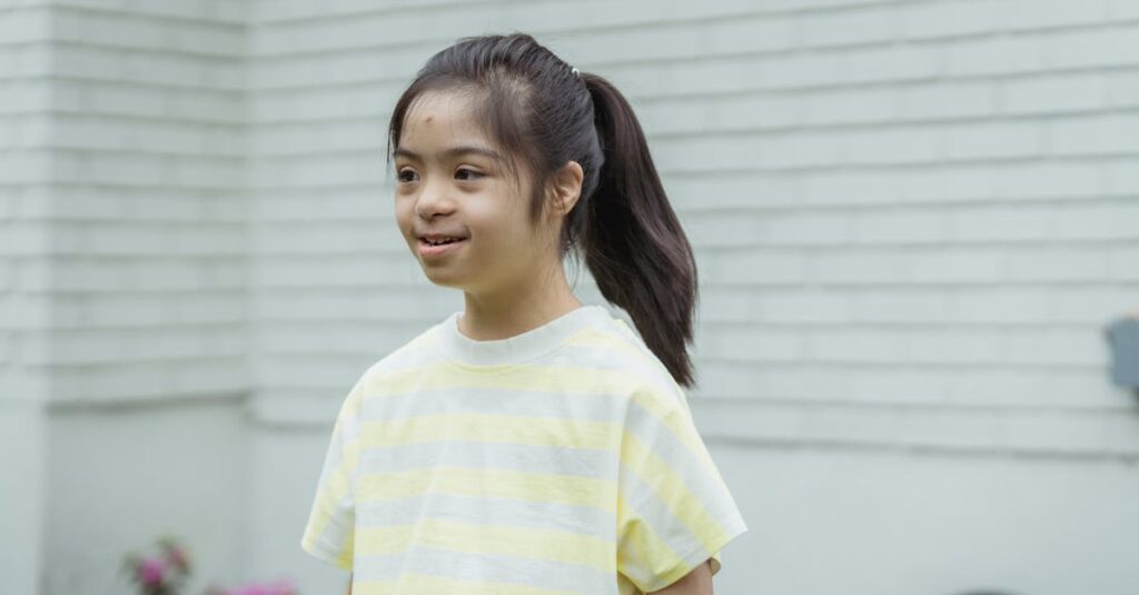 A happy young girl with Down syndrome smiling outdoors in a striped shirt with a ponytail.