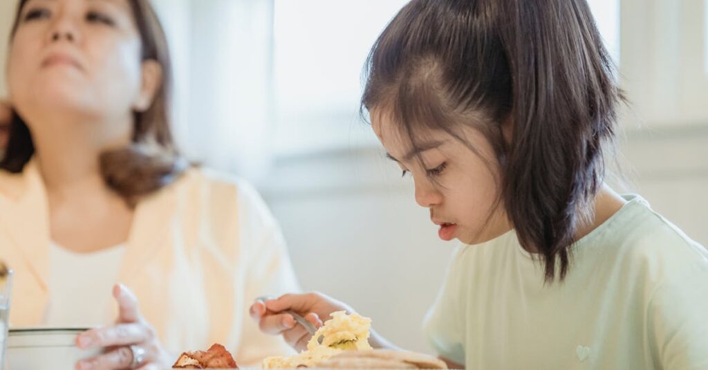 A young girl with Down syndrome enjoys breakfast with her mother in a cozy indoor setting.