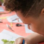 A young boy engaged in a drawing activity at an outdoor table with friends.