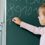 A girl engaging in educational learning by writing numbers on a chalkboard in a classroom.