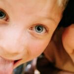 Two cheerful children having fun, making faces for a close-up selfie with joyful expressions.