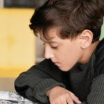 A young boy deeply focused on reading a comic book in a cozy indoor setting.
